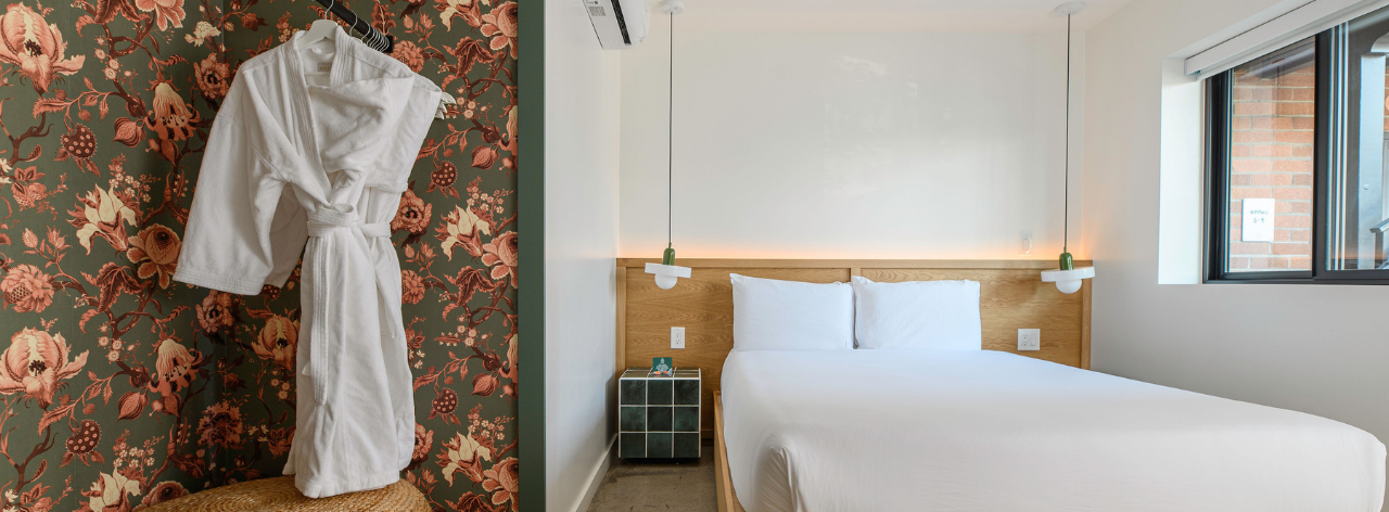 A hotel room with a bed, white robe hanging on the wall, and a window.